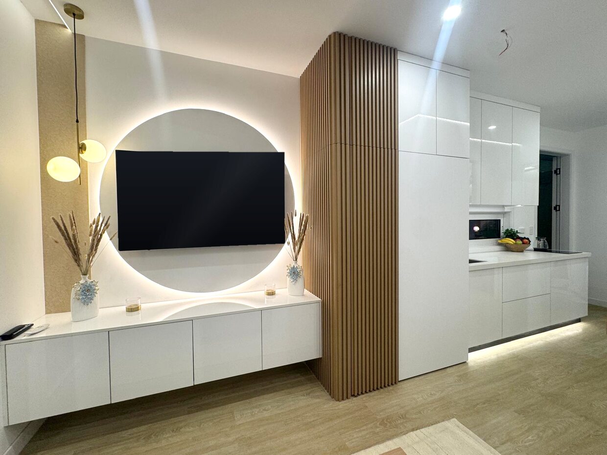 Inside the Generation 5 NOMI: floating TV cabinetry with a backlit circular feature wall, timber slat column and gloss white kitchen