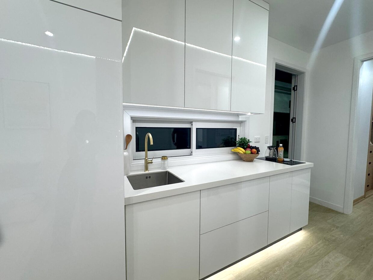Gloss white kitchen with stone benchtop, brass tap and window splashback